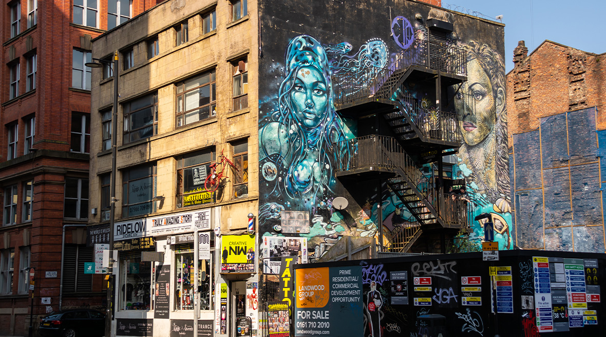 Brandtrappen aan de gevel van een flat met een muurschildering van twee figuren in blauw en zwart boven een winkel